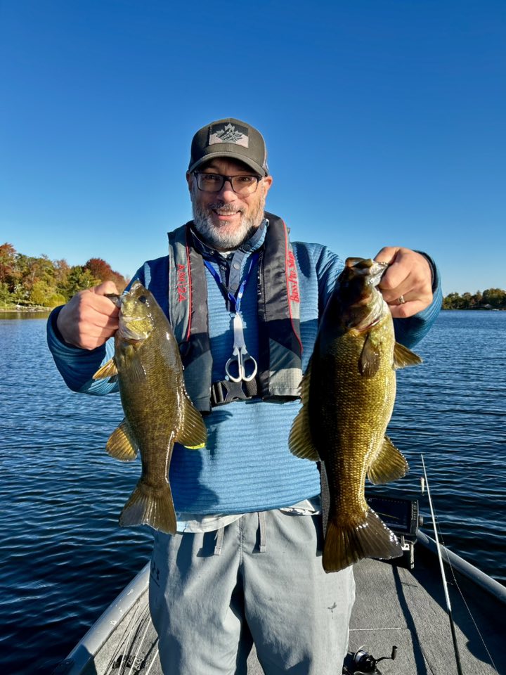 Guide holding 2 smallmouth bass while standing on boat
