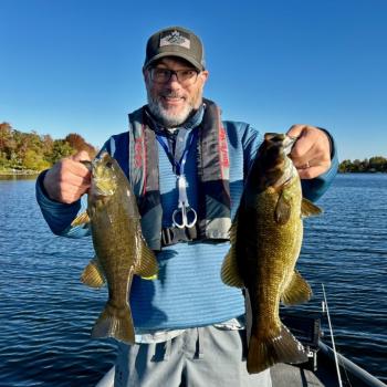 Guide holding 2 smallmouth bass while standing on boat